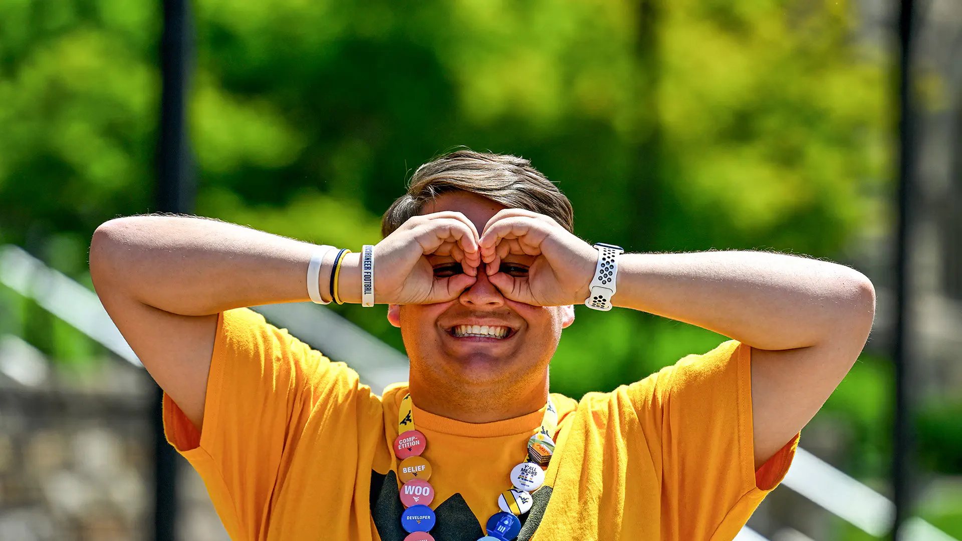 An orientation leader holding their hands up to their face like binoculars while wearing a lanyard full of student organization badges