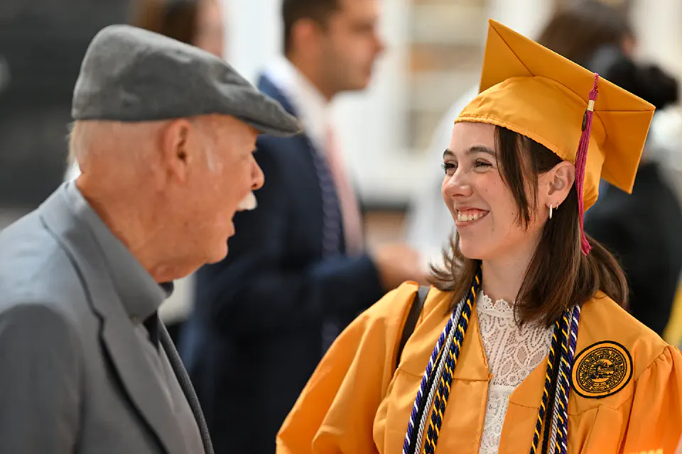 AN honors student wearing their graduation gown and smiling while talking to a family member 