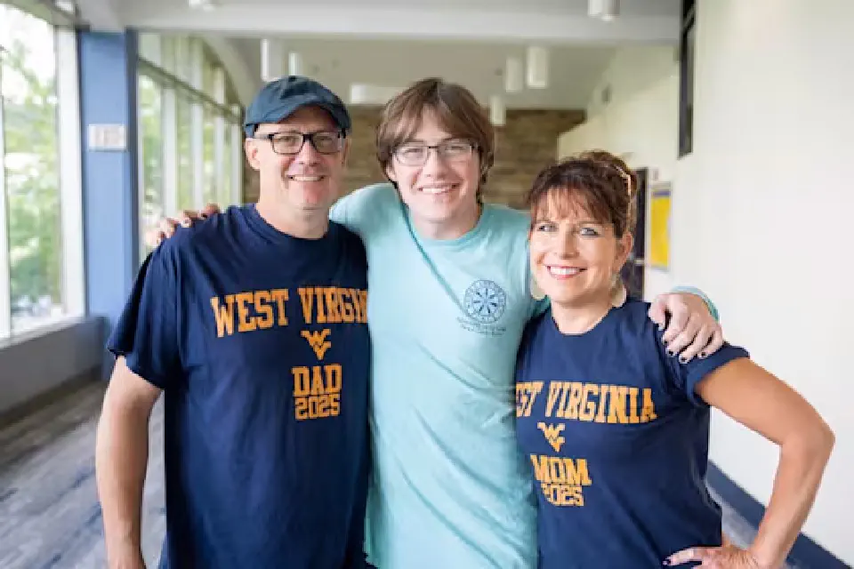 Parents wearing West Virginia Dad and West Virginia Mom shirts pose with their student.