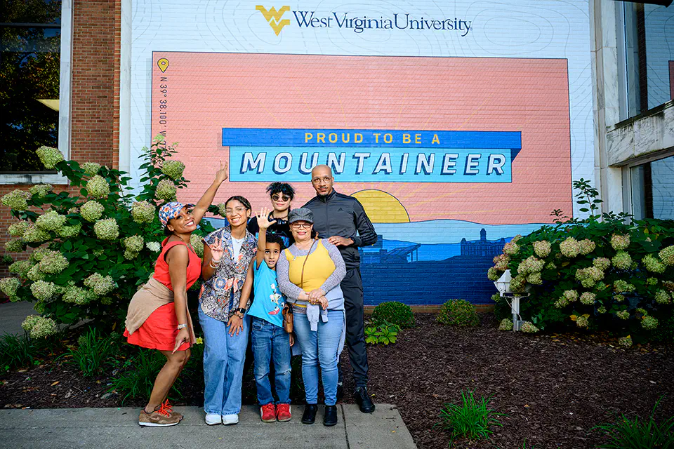 Family members pose with a WVU student for a photo in front of the Mountainlair mural