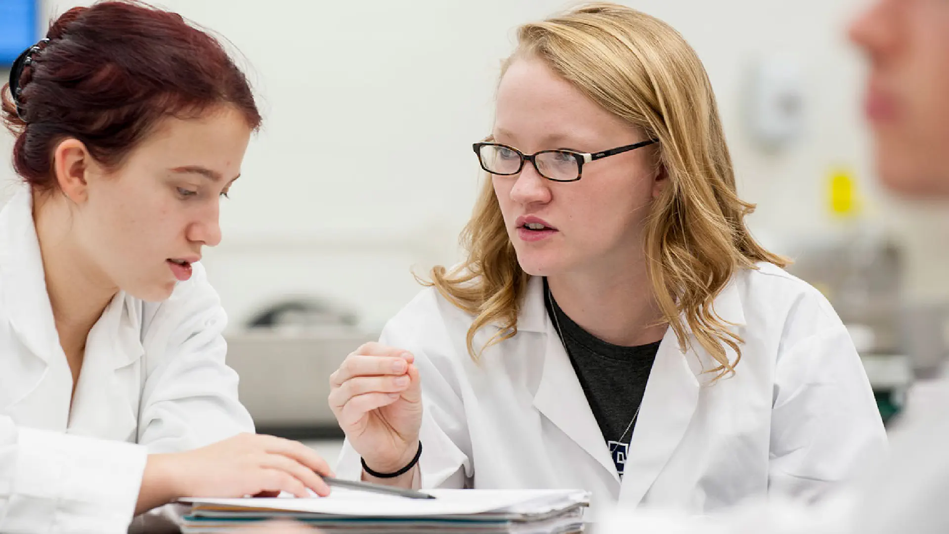 2 students wearing white lab coats look over notes